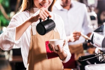 Asian Barista pouring milk to cup of coffee which is espresso with latte or cappuccino for customer order in coffee shop, Small business owner and startup in coffee shop and restaurant concept

