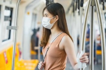 Young Asian woman passenger wearing surgical mask and hand touching with wet wipe in subway train when traveling in big city at Covid19 outbreak, Infection and Pandemic, new normal concept