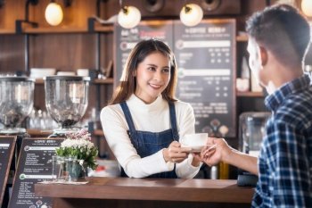 Asian Barista of Small business owner serving a cup of coffee to young customer at the coffee counter in coffee shop, Small business owner and startup in coffee shop and restaurant concept