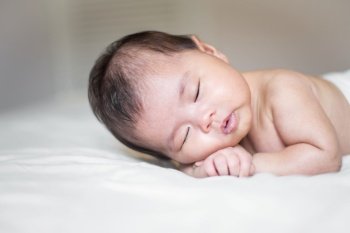 cute newborn baby is sleeping on white bed 