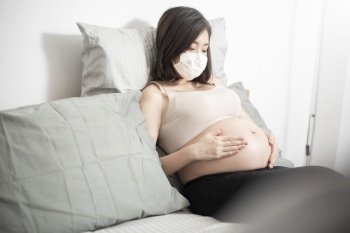  Beautiful asian pregnant woman is wearing protective mask in her home , Coronavirus protection concept 