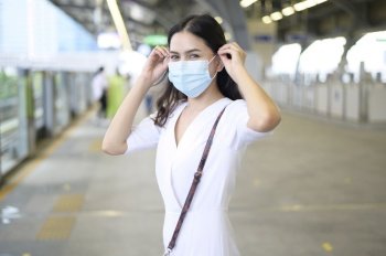 A young woman is standing on metro platform, wearing face mask , Covid-19 protection , New normal travel concept.. A young woman is standing on metro platform, wearing face mask , Covid-19 protection , New normal travel concept