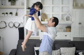 A healthy father is holding happy cute daughter flying and playing plane together at home on weekends, family concept. 