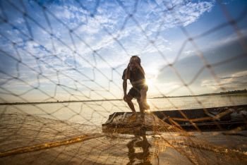 Asia fisherman net using on wooden boat casting net sunset or sunrise in the river - Silhouette fisherman boat with background life person countryside 