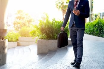 Businessman walking on the stairs and using smartphone outdoors.