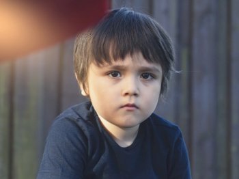 Emotional portrait of caucasian kid with thinking face with sunlight shining on his face, Upset little boy sitting alone in the park, Toddler with bored face looking out deep in thought.