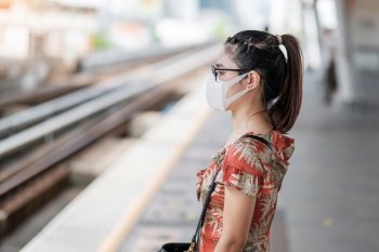 young Asian woman wearing Surgical face mask protect coronavirus inflection at public train station. social distancing, new normal and life after covid-19 pandemic