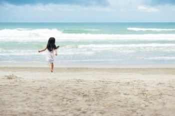 Little children girl black hair with white dress running playing with sand on a beach and wave sea