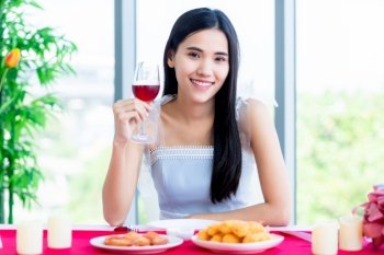 Valentine’s day concept, Happy of smiling Asian young female sitting at a table food show holding with wine glasses at in the restaurant background
