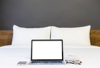 Laptop computer with blank white screen with smartphone,coffee cup and spectacles on white bed decoration in hotel bedroom interior background,Work and business in leisure with travel in the holiday.