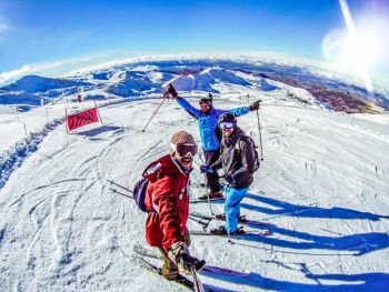 Skiers friends group taking fish eye selfie with gopro stick at snowy mountain top covered in snow skiing in Spain. Ski Winter sports with friend, holidays
