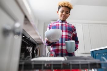 Boy Helping With Chores At Home By Stacking Crockery In Dishwasher