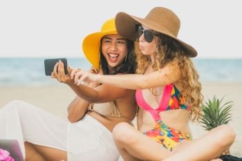 Happy women in bikinis taking selfie photograph from mobile phone together on tropical sand beach in summer vacation. Travel lifestyle.. Happy women taking photo on sand beach in summer.