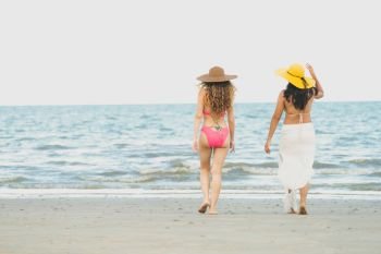 Happy women in bikinis go sunbathing together on tropical sand beach in summer vacation. Travel lifestyle.. Happy women go sunbathing at sand beach in summer.