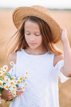 Portrait of adorable girl on summer day. Happy child in wheat field. Beautiful girl in white dress in a straw hat with ripe wheat in hands