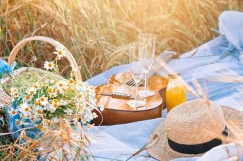 Closeup of picnic on nature in wheat field. Guitar, straw hat, wine with glasses and a basket of daisies. Closeup of picnic on nature in wheat field.