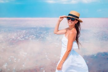 Portrait of woman on a pink salt lake with wind in her hair. Woman in hat walk on a pink salt lake on a sunny summer day.