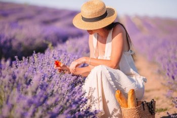 Beautiful young woman relaxing and having fun on purple flower lavender field. Woman in lavender flowers field at sunset in white dress and hat