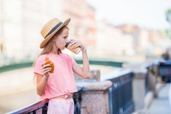 Beautiful little tourist girl with a croissant and coffee outdoors on the promenade on the river. Woman with a croissant and coffee outdoors on the promenade