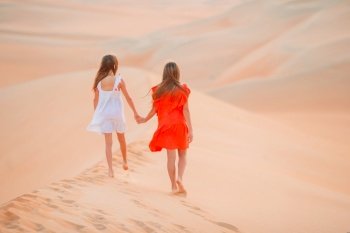 Little beautiful girls among dunes in big sandy desert walking. Girls among dunes in Rub al-Khali desert in United Arab Emirates