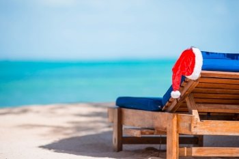 Santa Claus Hat on beach lounger with turquoise sea water and white sand. Christmas vacation concept. Sun loungers with Santa Hat at beautiful tropical beach with white sand and turquoise water. Perfect Christmas vacation