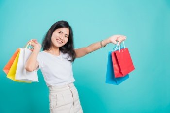 Portrait happy Asian beautiful young woman standing wear white t-shirt, She holding shopping bags multi color on hand and looking to camera, shoot photo in a studio on a blue background