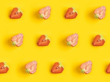 Diagonal pattern from ripe juicy strawberries cut in half on bright yellow background. Creative minimalist flat lay. Vitamins vegan healthy diet concept. 