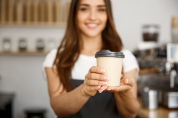 Coffee Business Concept - Beautiful Caucasian lady smiling at camera offers disposable take away hot coffee at the modern coffee shop