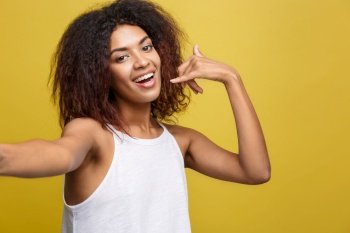 Close-up Cheerful young beatiful African American woman taking a selfie herself and make phone symbol by hand. Yellow studio background. Copy Space. Close-up Cheerful young beatiful African American woman taking a selfie herself and make phone symbol by hand. Yellow studio background. Copy Space.