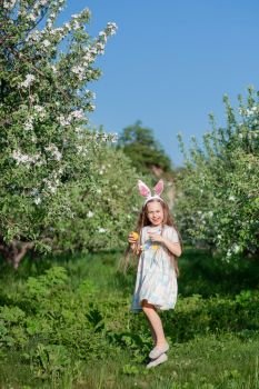 Cute girl with bunny ears on Easter day. A girl is chasing Easter eggs in the garden. The girl has a basket with painted eggs.. Cute girl with bunny ears on Easter day. A girl is chasing Easter eggs in the garden.