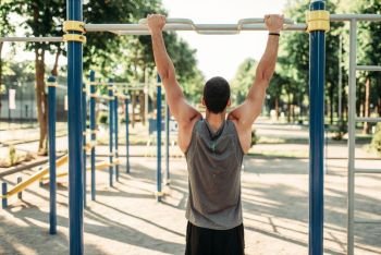 Athletic man doing exercise on horizontal bar on outdoor fitness workout. Strong sportsman on sport training in park. Man doing exercise on horizontal bar outdoor