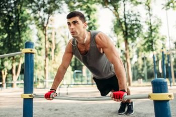 Athletic man doing push-up exercise using horizontal bar, outdoor fitness workout. Strong sportsman on sport training in park. Man doing push-up exercise using horizontal bar