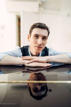 Male pianist at the classical black grand piano with perfectly polished surface. Performer poses at the royale keyboard, musical instrument. Pianist at the piano, perfectly polished surface