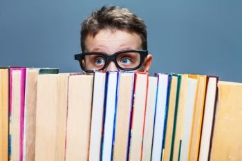 Little schoolboy in glasses peeking from behind the books. Education concept