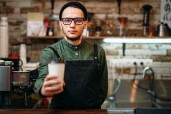 Barman in black apron stretches plastic cup of coffee in hands.. Barman in black apron stretches plastic cup