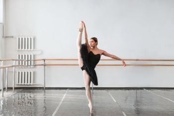 Skill female ballet dancer shows stretching in class, barrre and white wall on background