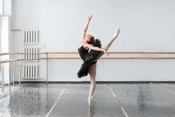 Skill female ballet dancer shows stretching in class, barrre and white wall on background. Skill ballet dancer shows stretching in class