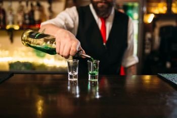 Barkeeper pouring alcoholic beverage in glass behind restaurant bar counter