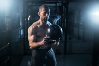 Strong weightlifter workout with kettlebell in gym. Man with muscular torso training with weight. Strong weightlifter workout with weight in gym