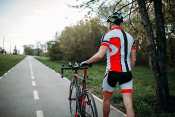 Cyclist in helmet and sportswear rides on bicycle, back view. Workout on bike path, cycling. Cyclist in helmet and sportswear rides on bicycle