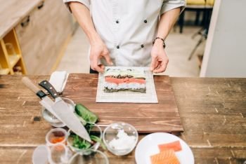 Male cook making sushi on wooden table, asian kitchen preparation process. Traditional japanese cuisine, seafood. Male cook making sushi, asian kitchen