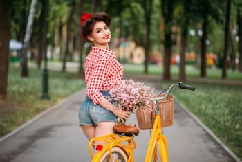 Pinup girl on retro bicycle with backet of flowers. Pin-up style pretty woman. Pinup girl on retro bicycle with backet of flowers