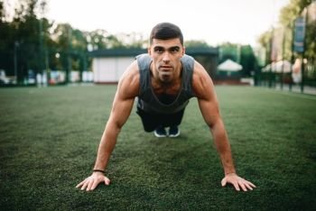 Male athlete doing push-up exercise on outdoor fitness workout. Sportsman on the training in park. Athlete doing push-up exercise on outdoor workout