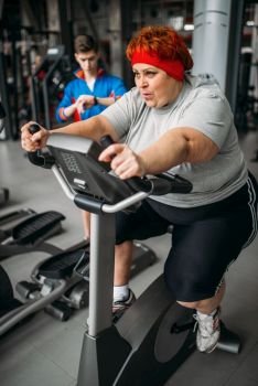 Overweight woman, workout on exercise bike in gym. Calories burning, obese female person in sport club, fat people