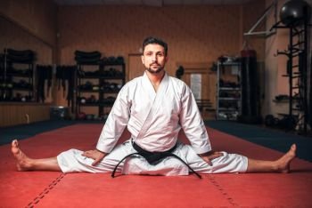 Martial arts karate master in white kimono and black belt doing stretching exercise in gym. Martial arts master doing stretching exercise