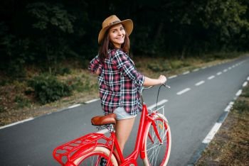 Portrait of young pretty woman in hat with red vintage bicycle, green summer park. Cycling outdoor. Girl on retro cycle. Portrait of pretty woman with red vintage bicycle