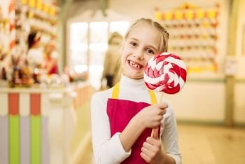 Happy little girl holds handmade sugar caramel on stick. Fresh lollipop in candy store