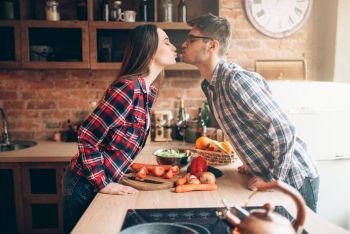 Happy couple kissing while preparing a romantic dinner. Vegetable salad preparation. Family prepares healthy food on the kitchen
