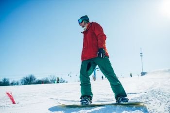 Snowboarder in glasses poses with board in hands, blue sky and snowy mountains on background. Snowboarder in glasses poses with board in hands