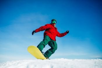 Snowboarder in glasses poses with board in hands, blue sky and snowy mountains on background. Winter active sport, extreme lifestyle, snowboarding. Snowboarder in glasses poses with board in hands